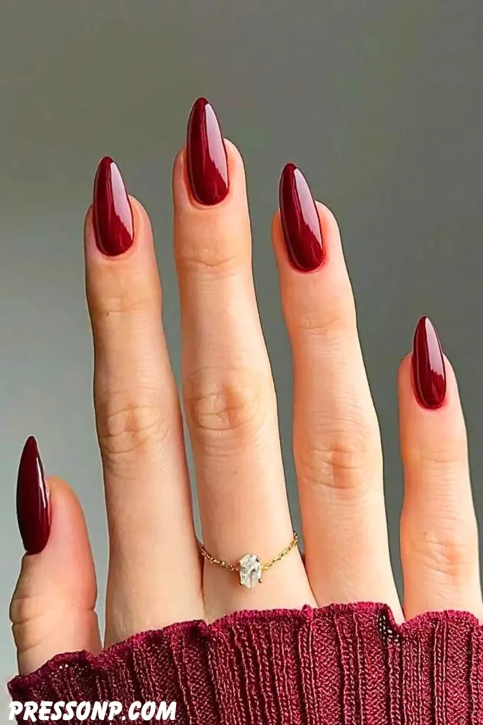 A close-up of a hand with long, elegant almond-shaped nails coated in a rich, high-gloss solid cherry red polish.