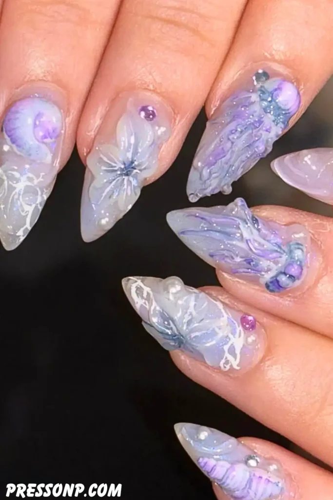 A close-up of stiletto-shaped nails featuring highly detailed, 3D sculpted translucent nail art in shades of lavender, violet, and iridescent pearl with sea life motifs.