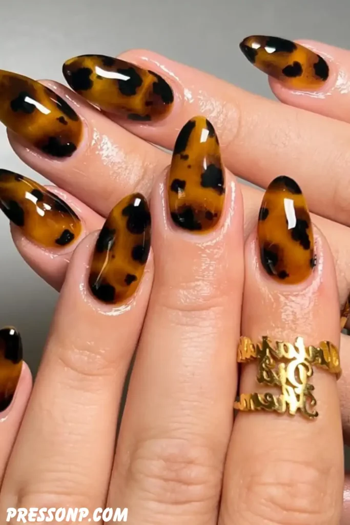 A close-up of a hand with short, round nails featuring a retro-inspired mix of semi-translucent amber tortoiseshell patterns and solid, warm mustard yellow polish.