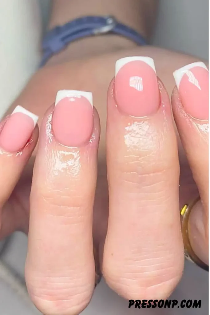 A close-up of a hand with neat, square-shaped nails featuring a timeless French manicure with a glossy sheer pink base and crisp white tips.
