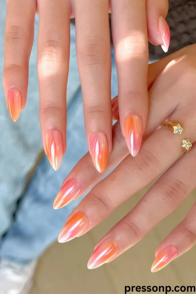 A close-up of long, almond-shaped extension nails featuring a glossy, iridescent chrome finish that blends shades of warm coral orange and sunset pink.