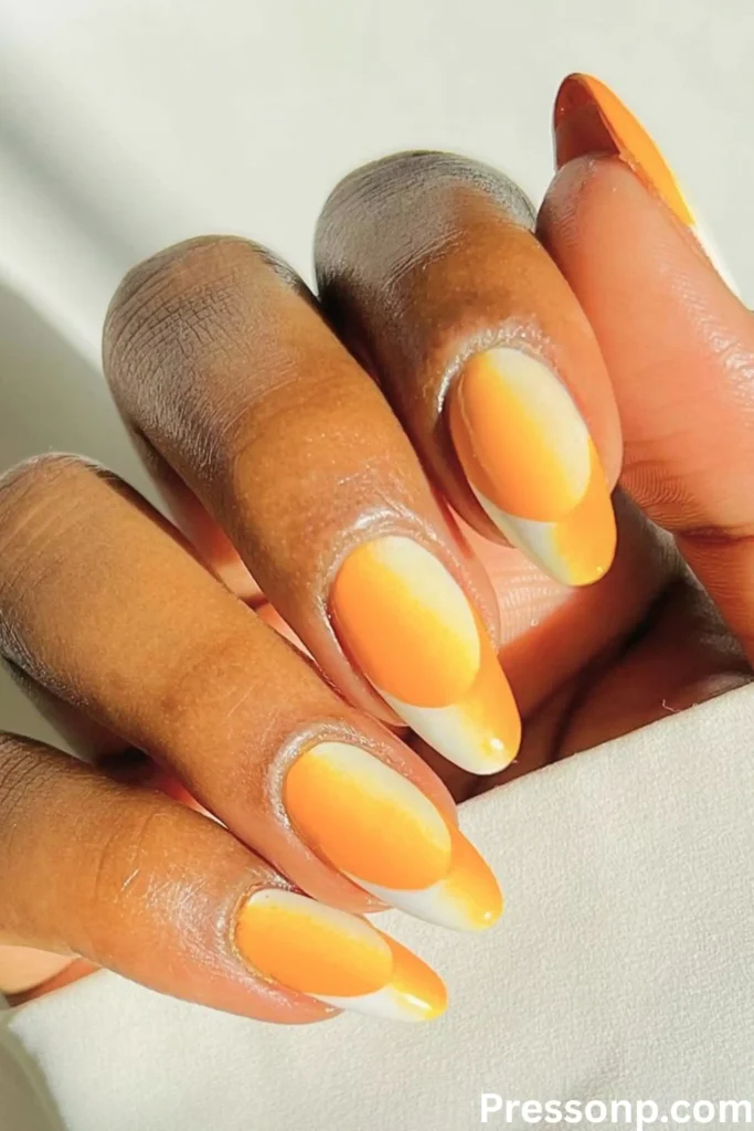 A close-up of a hand with almond-shaped nails featuring a bright orange and white "sand-to-sea" ombré gradient.