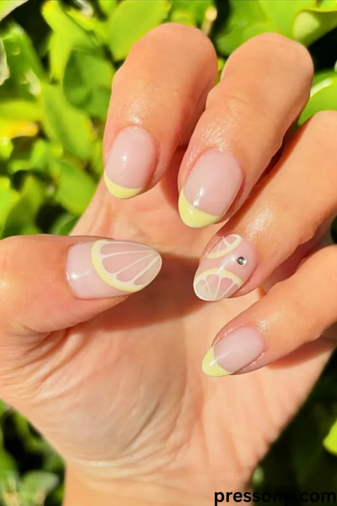 A close-up of a hand displaying short, oval-shaped nails with a glossy nude base, featuring pastel yellow French tips and hand-painted translucent lemon slice nail art.