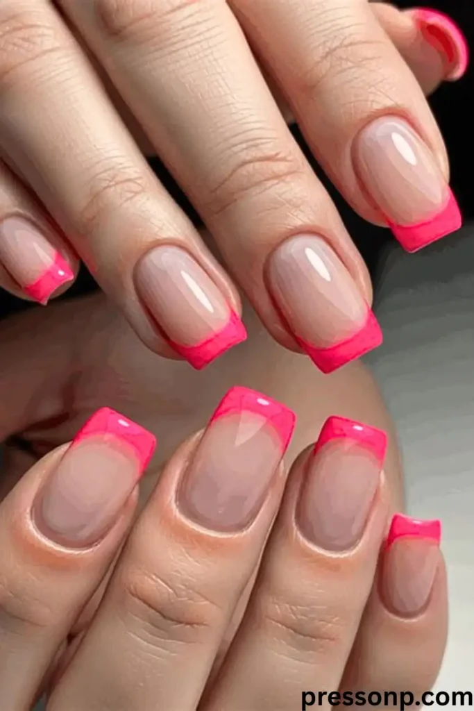 "A close-up of a sophisticated manicure featuring medium-length square nails. The design showcases a classic French tip reimagined with a punchy hot pink polish. The vibrant neon tips contrast sharply against a clean, glossy nude base, offering a bold and energetic take on a traditional summer nail style."