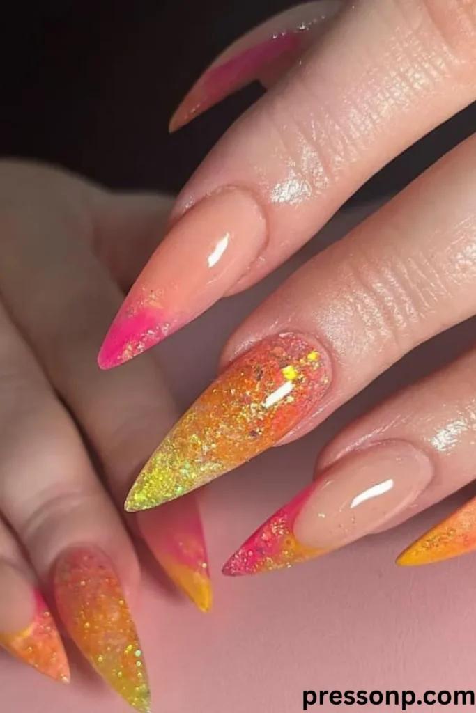 A close-up of hands showcasing long, sharp stiletto acrylic extensions with a high-gloss finish, featuring a mix of full-coverage iridescent orange-yellow glitter nails and nude negative-space nails with vibrant pink and yellow French tips