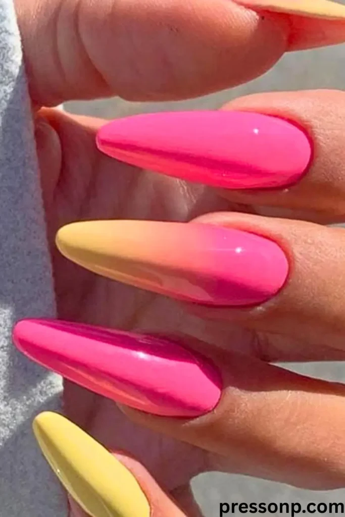 A close-up of "Ombré Neon Summer Nails – Two Colors, One Wow" featuring long, pointed stiletto-shaped nails. The design showcases a seamless gradient transition from bright neon pink at the base to a sunny yellow at the tips. The high-gloss finish reflects the sunlight, emphasizing the bold, electric summer vibe of the two-tone look.