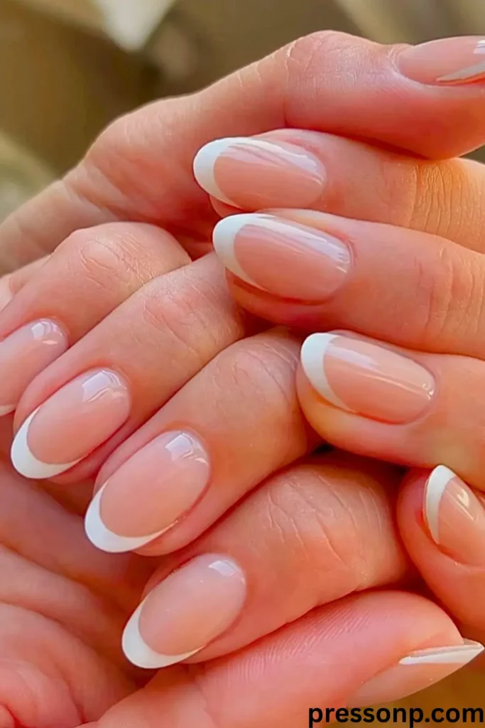 A close-up, sunlit photograph of a hand showcasing low-maintenance, medium-length round nails polished in a clean, high-gloss semi-translucent jelly pink.