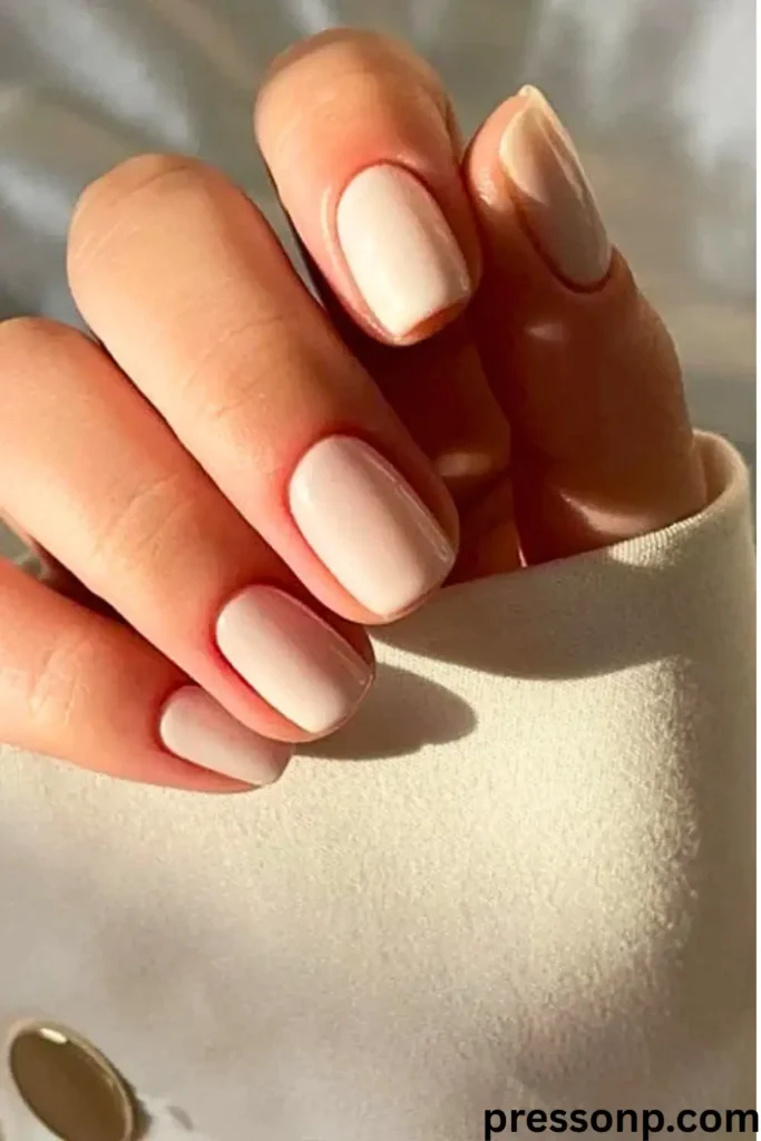 A close-up of two hands loosely clasped together, showcasing a timeless and elegant French manicure on medium-length, perfectly sculpted round-oval nails.
