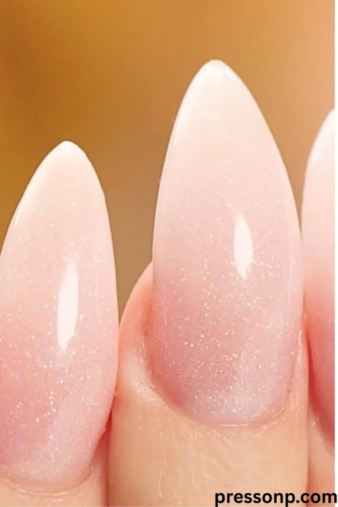 A close-up of a hand with long, elegant oval-round nails showcasing a glossy pink-to-white ombre baby boomer manicure.