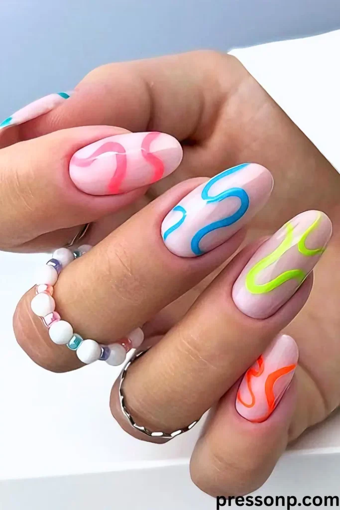 A hand featuring "Retro 90s Neon Summer Nails with Squiggles" on oval-shaped nails with a milky white base. Each nail displays a vibrant, 3D-textured squiggle in a different neon color: hot pink, electric blue, lime green, and bright orange. The playful look is accessorized with a white and pastel beaded ring, capturing a fun and nostalgic summer aesthetic.