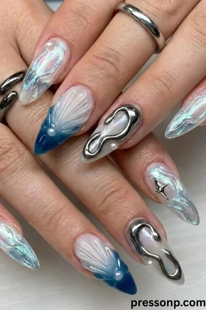 A close-up of hands displaying long, stiletto-shaped extensions with an iridescent sea-glass base, adorned with 3D sculpted ocean wave seashells, raised metallic liquid silver squiggles, and delicate pearl embellishments.