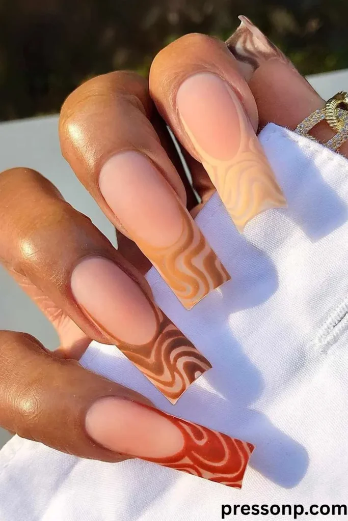 A close-up of a hand showcasing extra-long, square-shaped nails with a matte nude base and an abstract French tip design featuring swirling, retro squiggles in a gradient of warm brown, tan, and terracotta shades.