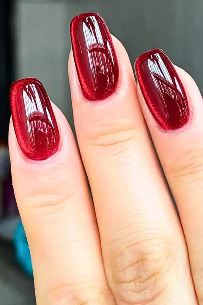 "Close-up of long, square-shaped nails featuring a deep cherry red jelly finish. The polish has a high-shine, translucent 'syrup' effect with a subtle velvet-like shimmer underneath, showcasing the 'Juicy Jelly' trend for Summer 2026."