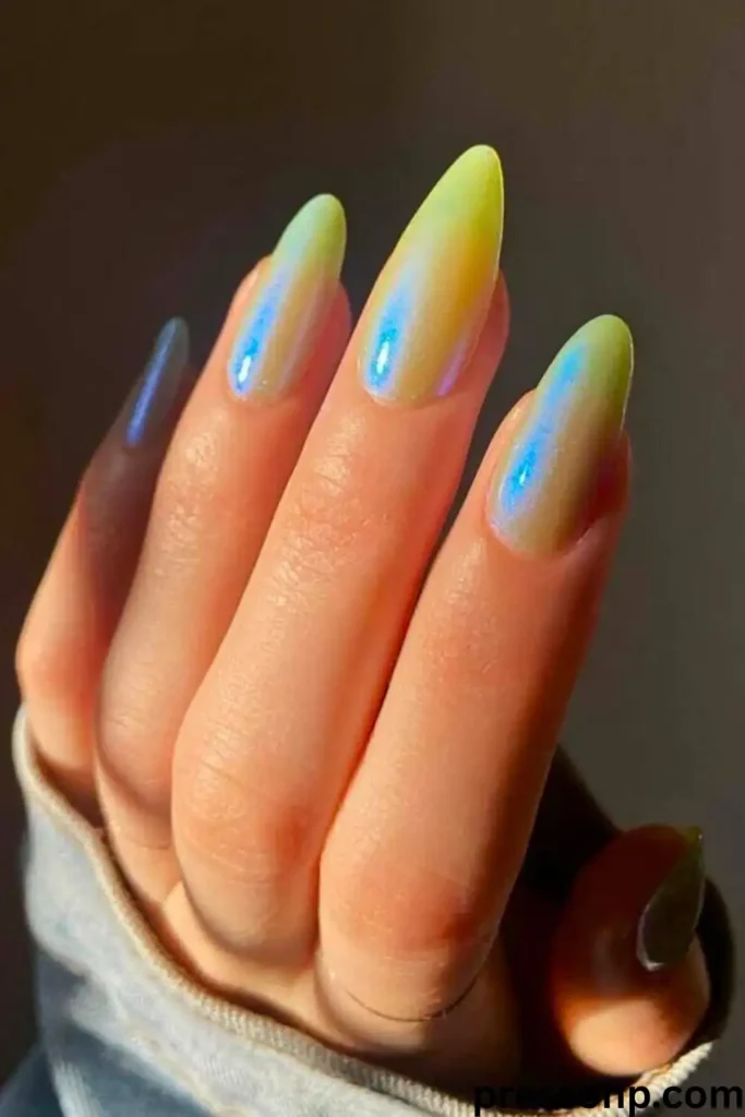 A close-up of a hand with long, elegant almond-shaped nails coated in a translucent, jelly-like neon lime yellow base overlaid with a striking electric blue iridescent chrome shimmer.