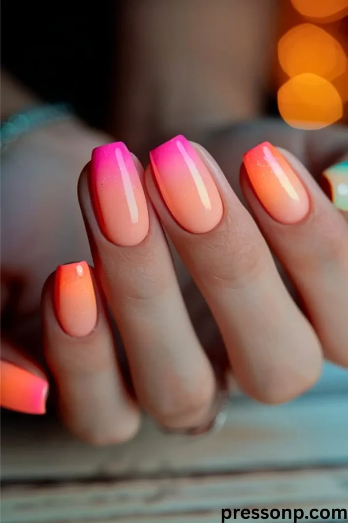 A close-up of medium-length square nails showcasing a smooth, vibrant summer ombré gradient that transitions from bright neon pink at the tips to a warm peach-orange at the base.