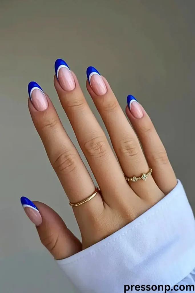 close-up of a hand with long, elegant almond-shaped nails featuring a clean, semi-translucent nude base and a bold double French tip design in vibrant cobalt blue and crisp white.
