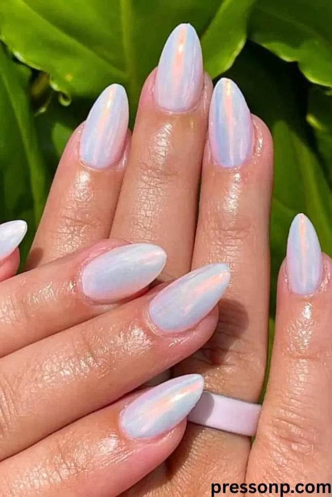 A close-up of hands under bright sunlight showcasing long almond-shaped nails coated in a high-gloss, translucent white pearlescent chrome lacquer with a luminous orange-pink reflection.