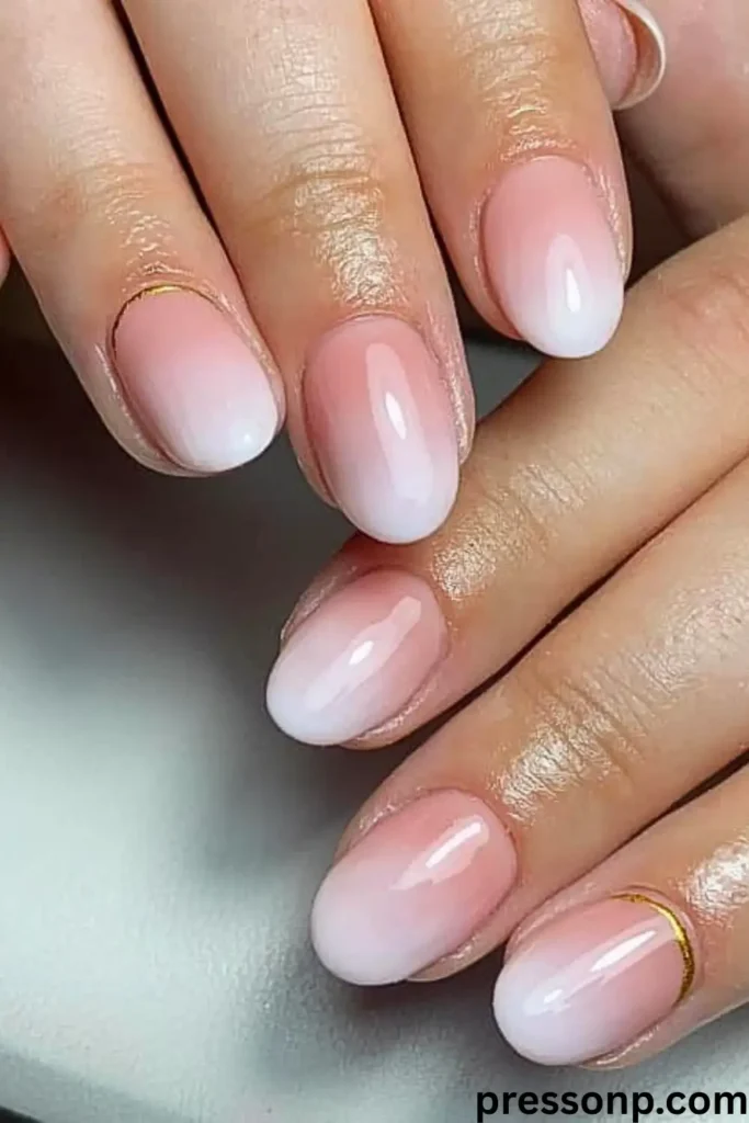 A close-up of short, neatly rounded nails featuring a flawless neutral French ombré gradient that fades smoothly from a soft nude base to milky white tips, accented with a delicate gold foil crescent at the cuticles.