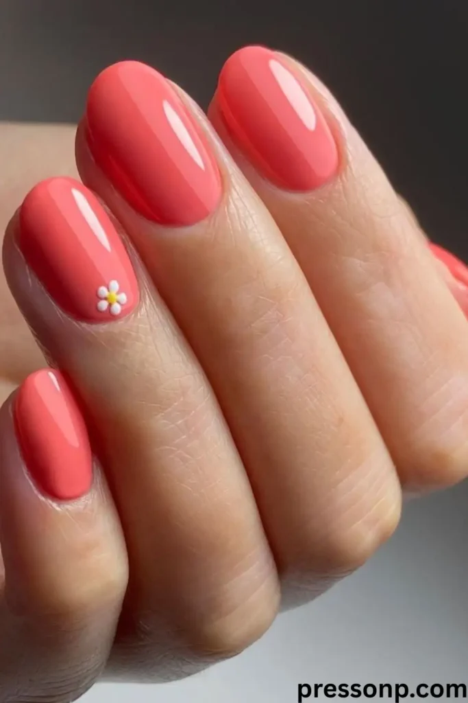 A close-up of a hand showcasing medium-length, square-shaped nails painted in a vibrant, high-gloss solid coral pink lacquer.