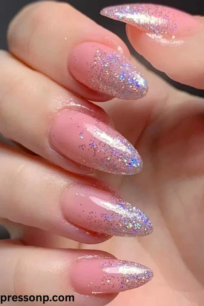 A close-up of long, almond-shaped nails coated in a glossy bubblegum pink base, featuring a sparkling silver holographic glitter gradient concentrated at the tips.