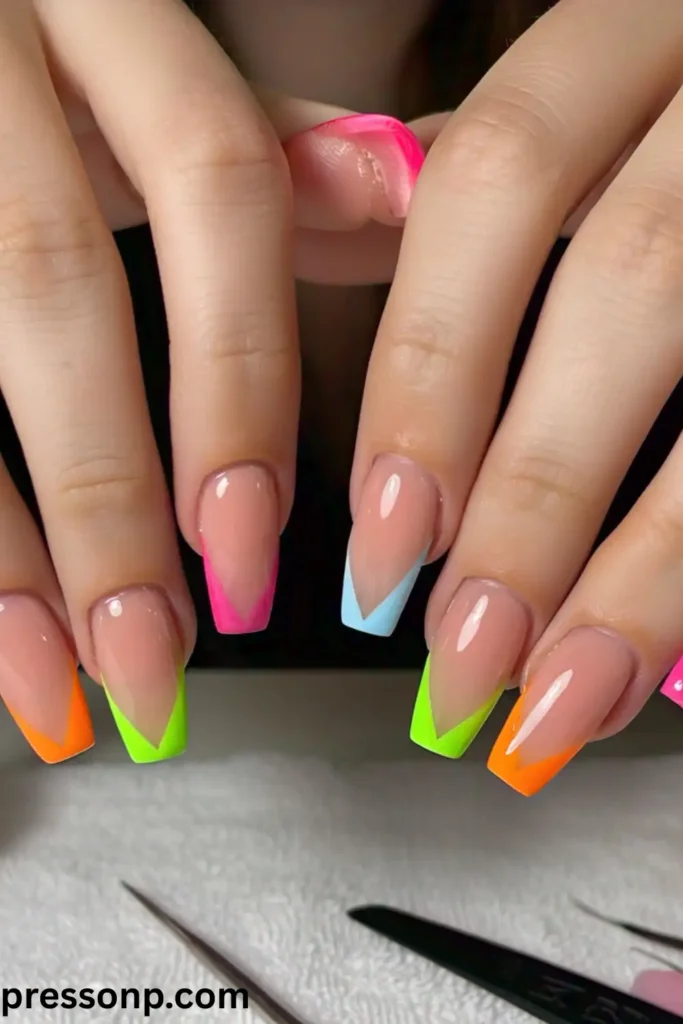 A close-up of long, square nails featuring a clean nude base coat accented with sharp, geometric V-shaped French tips in various neon shades like pink, orange, lime green, and baby blue.