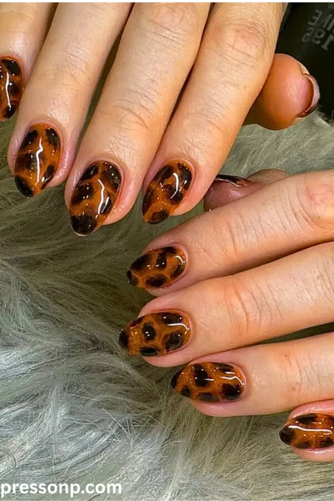 A close-up of hands displaying an ultra-glossy, semi-translucent tortoise shell manicure on natural oval-shaped nails, featuring rich amber, caramel, and dark brown layered tones