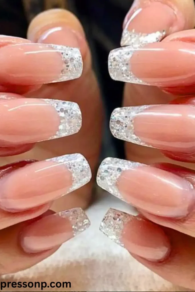 A close-up of long, sculpted square nails featuring a sheer nude base coat with thick, bold French tips packed with chunky, reflective silver glitter.