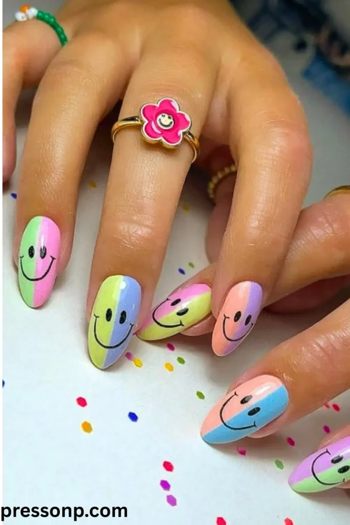 A close-up of almond-shaped nails featuring a split two-tone pastel color base on each finger, topped with classic black hand-painted retro smiley faces.