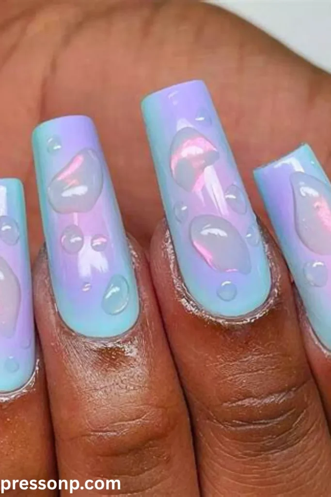 A close-up of long, square-shaped nails with a iridescent pastel blue and purple gradient base, decorated with realistic 3D clear gel droplets that look like fresh rainwater.