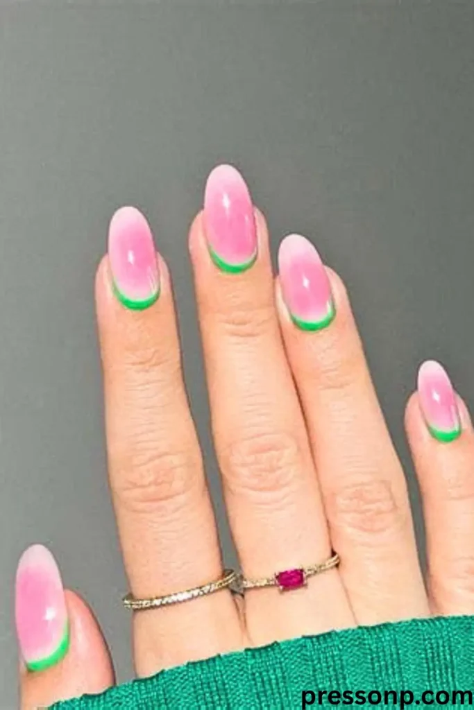 A close-up of a hand with long, oval nails featuring a "Neon Reverse French" manicure. The design shows a soft pink aura center with a bright neon green crescent painted precisely at the cuticle line.