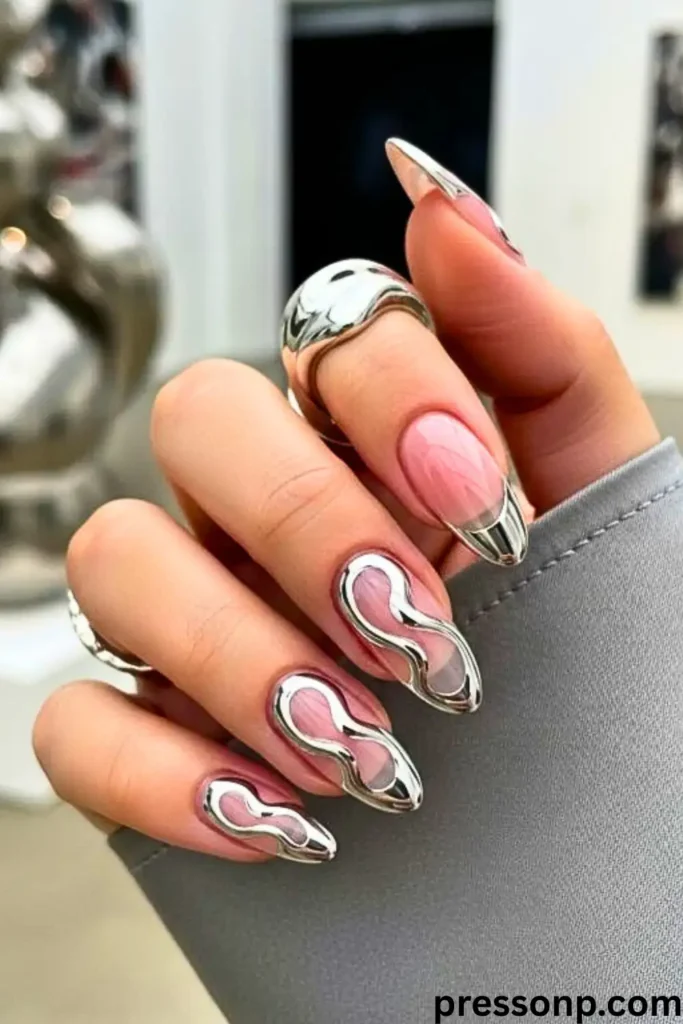 A close-up of long, almond-shaped nails featuring a "Liquid Metal Magic" manicure with high-shine, 3D molten silver chrome swirls over a sheer pink base.