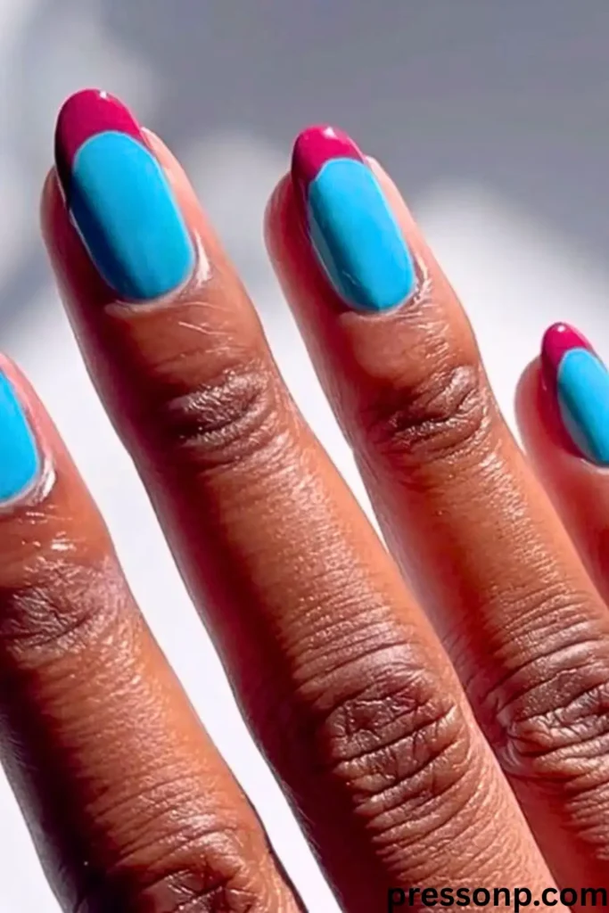 A close-up of a hand featuring a "Color-Blocked French" manicure with long, rounded nails painted in bright turquoise blue and capped with thick, contrasting magenta tips.