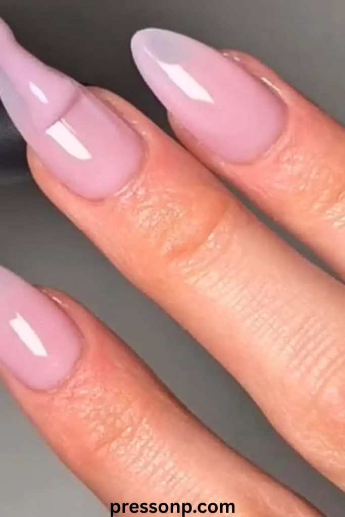 A close-up of long, square-shaped nails featuring a high-gloss, sheer pink "milky glaze" manicure that mimics a clean, natural look.
