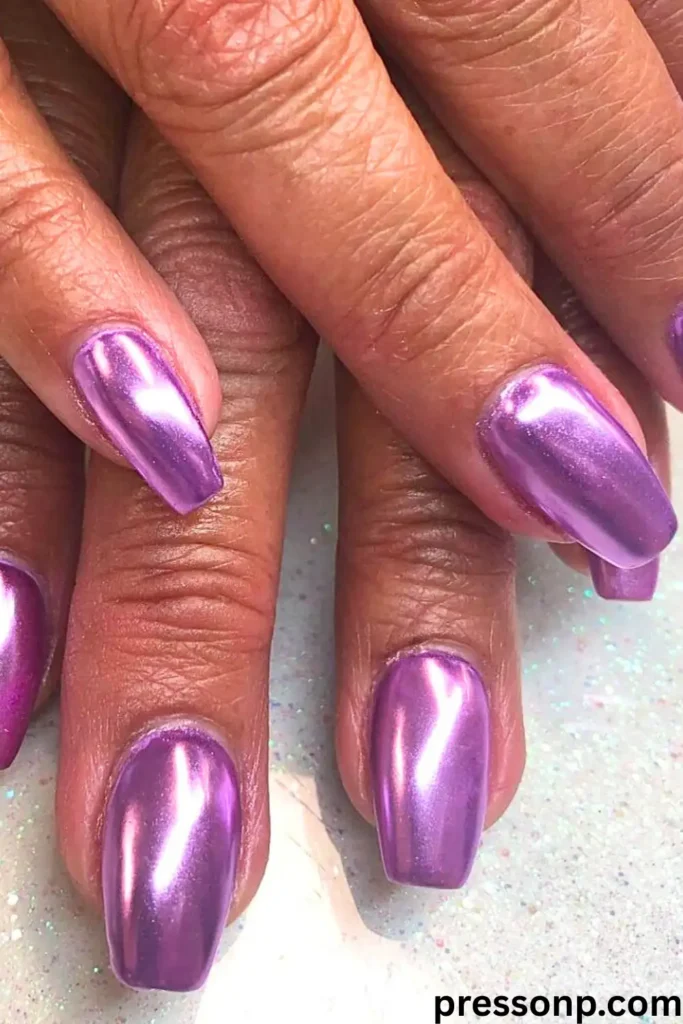 A close-up of hands featuring a "Lavender Chrome" manicure with medium, square-shaped nails finished in a high-shine, metallic purple chrome.