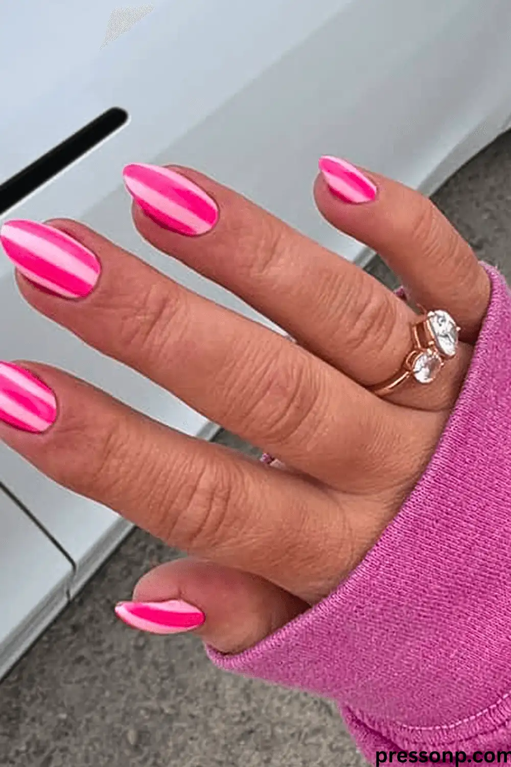 A close-up of a hand with long, oval nails featuring a fun "Candy Stripe" manicure with bold, alternating vertical stripes of vibrant hot pink and soft baby pink.