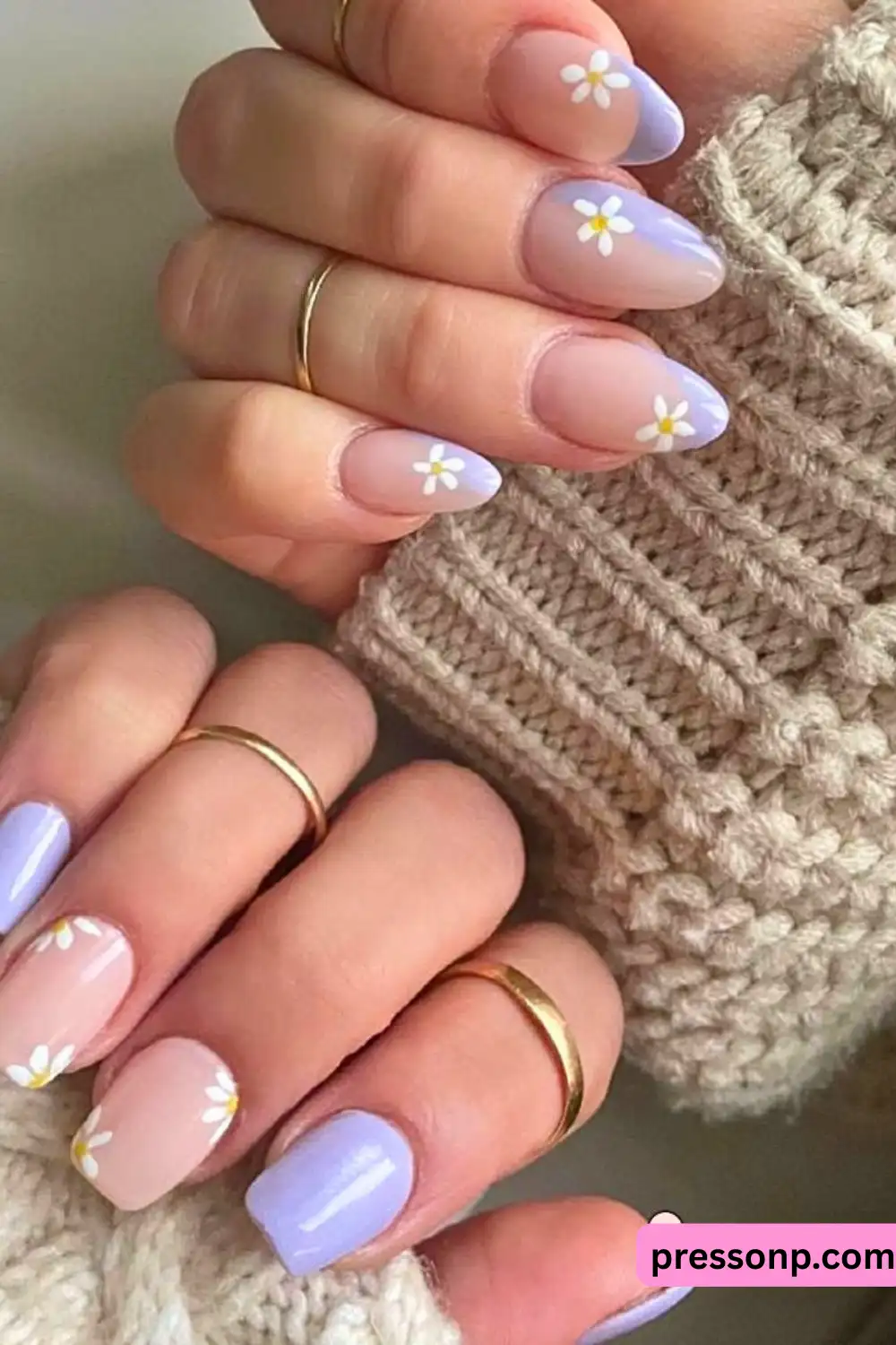 A close-up of hands featuring a cottagecore-inspired manicure with sheer pink and pastel lavender nails decorated with delicate white daisy flower accents.