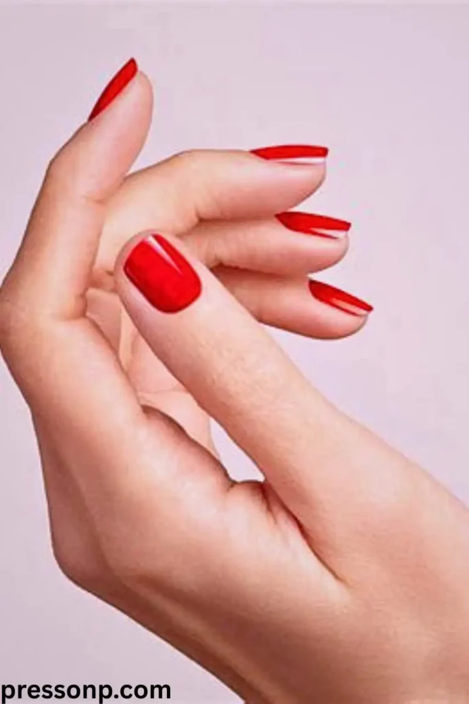 "A close-up of a hand with olive skin and neutral undertones featuring medium-length, square-shaped nails in a classic vibrant poppy red. The bright, balanced red shade provides a stunning pop of color that enhances the green and gold depths of olive skin tones. The pressonp.com watermark is visible in the bottom left corner."