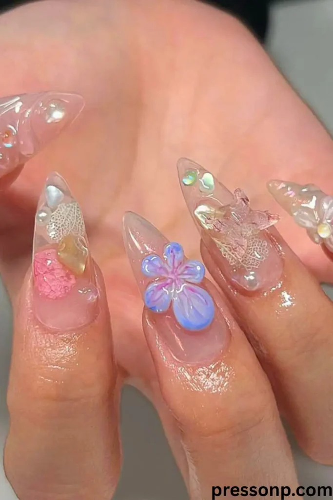 A close-up of long, square-tapered acrylic nails featuring a clear, encapsulated design embedded with real, vibrant pink 3D pressed flowers and delicate gold leaf flakes.