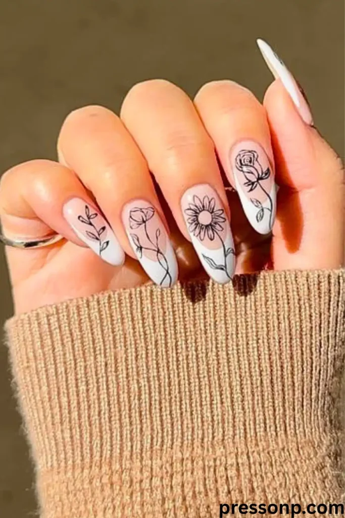 A close-up of a hand with long, almond-shaped nails featuring a modern white French manicure decorated with delicate black ink line art illustrations of botanical stems and flowers.