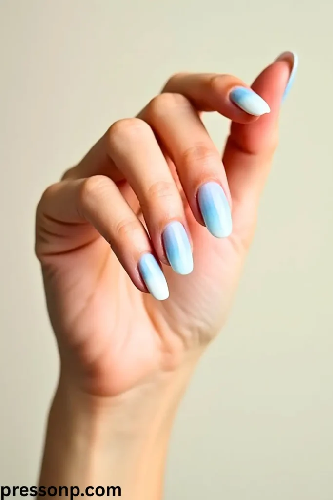 A close-up of a hand with long, oval nails featuring a dreamy, translucent base that seamlessly fades into a glittering mint-green and cool emerald ombre effect at the tips.