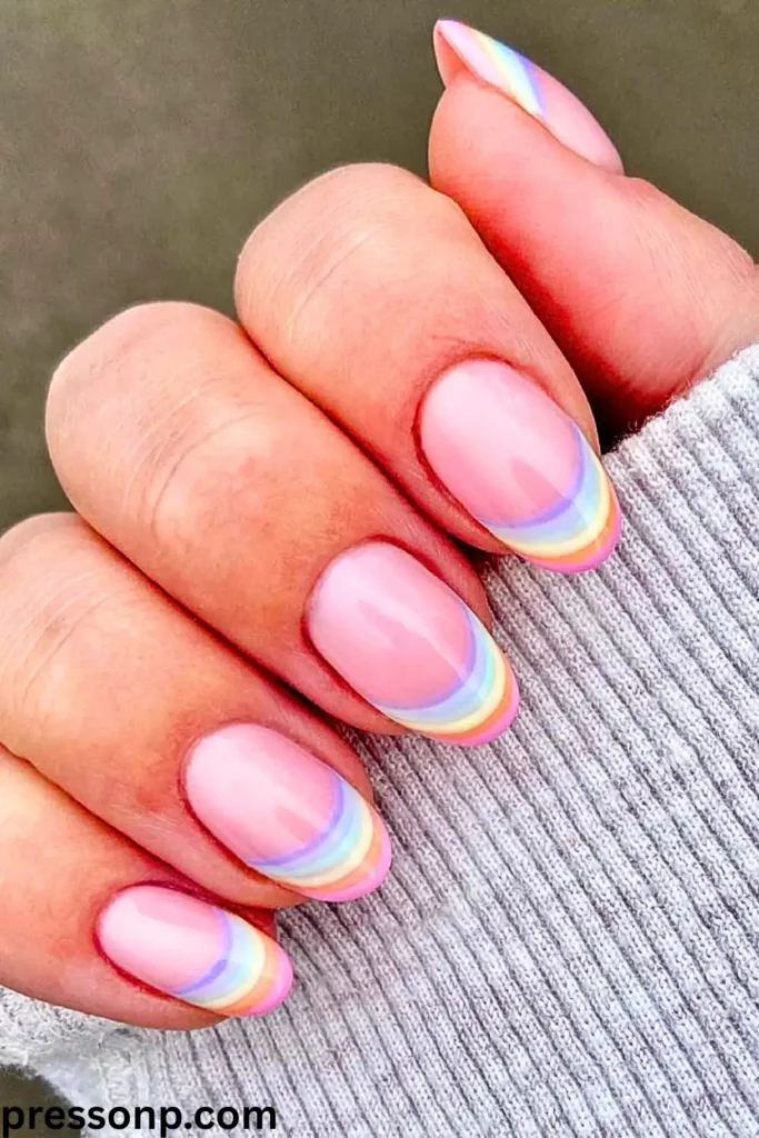 A close-up of a hand with medium-length oval nails displaying a creative rainbow French manicure remix, featuring multi-colored pastel arched tips over a glossy sheer pink base.