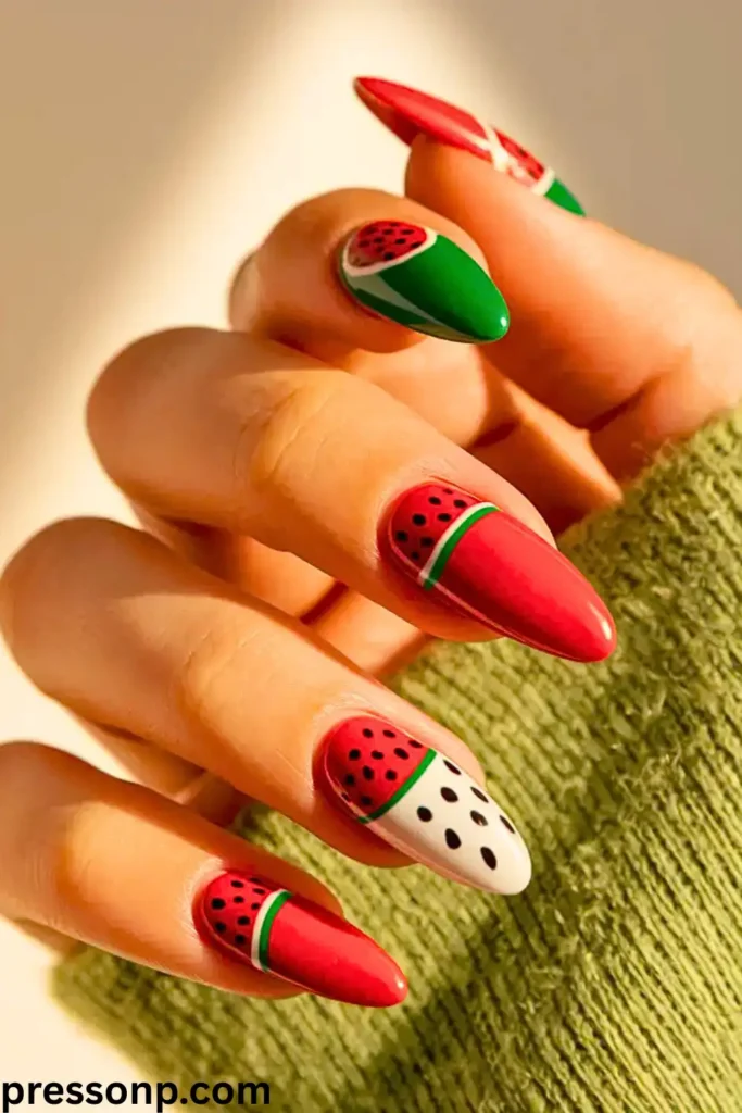 A close-up of a hand with short, round nails featuring a playful fruit-themed manicure that combines vibrant hot pink nails with clear accent nails decorated with tiny, realistic polymer watermelon slices.