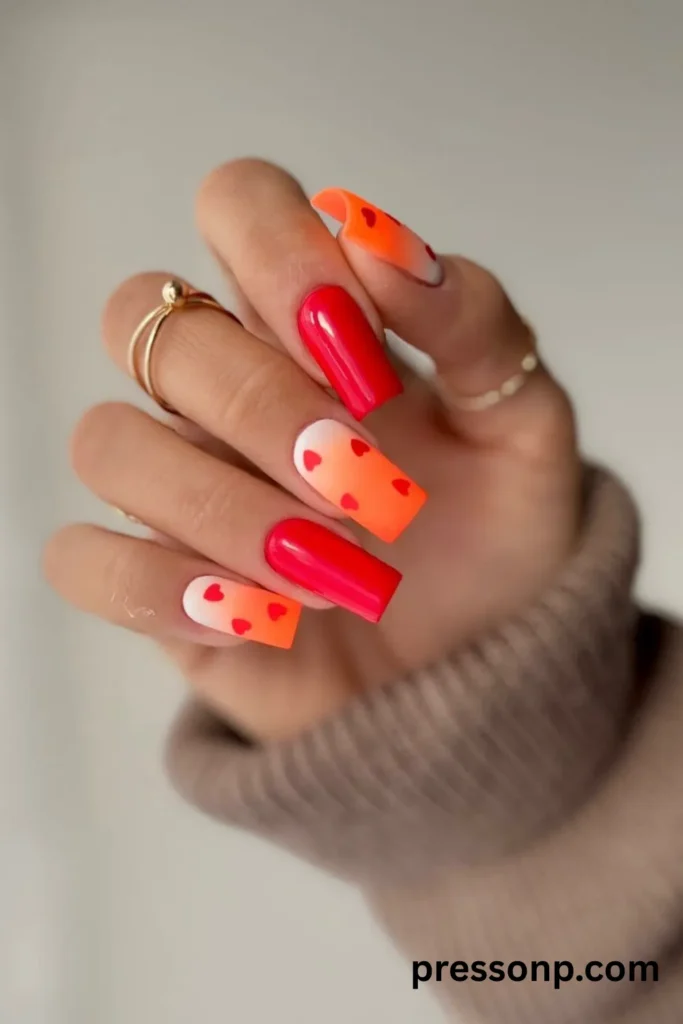 Long square ombre nails with a vibrant neon orange and white gradient base, decorated with small hand-painted red hearts.