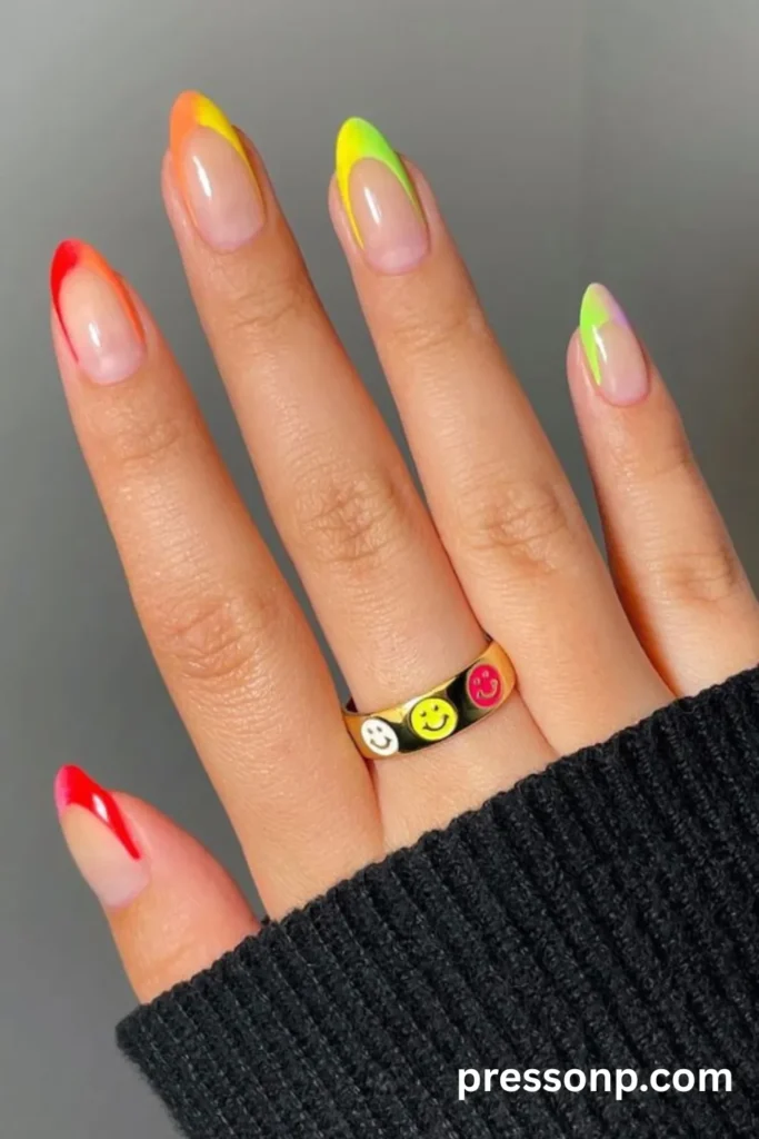 Long oval French manicure with a gradient of neon colors on the tips and a gold smiley face ring.