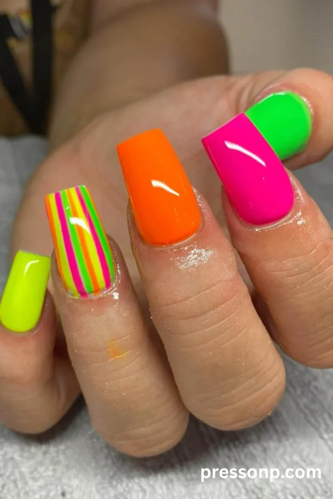 Long coffin nails with a mix of solid neon green, orange, pink, and bright multi-colored vertical stripes.