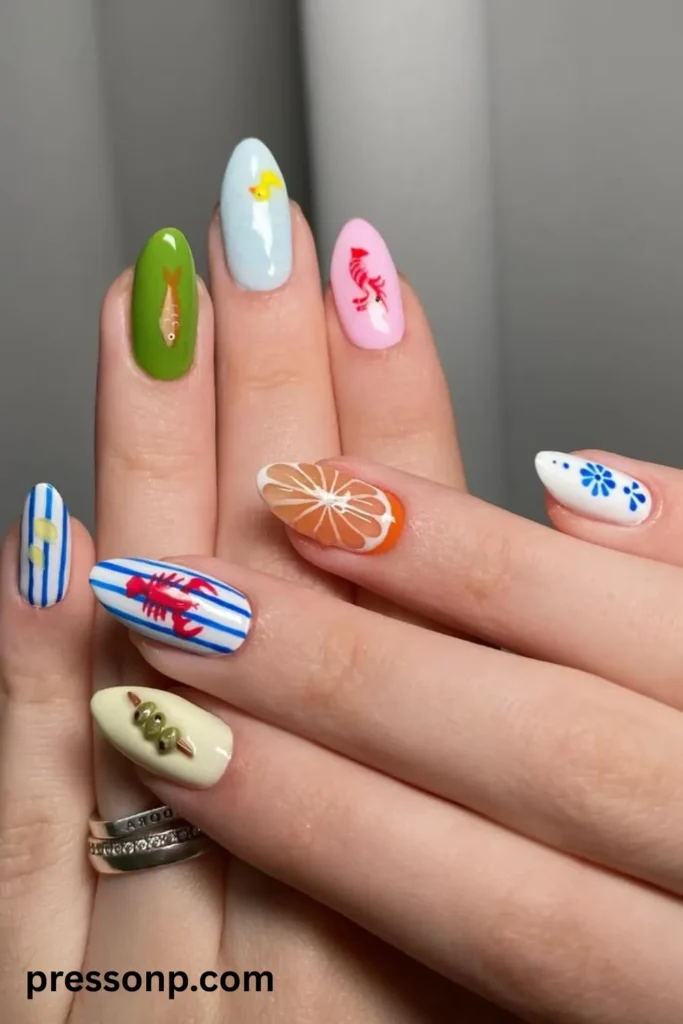 A close-up of two hands showing a playful, mismatched Mediterranean holiday manicure on medium almond nails, featuring blue-and-white stripes with a red lobster, an orange citrus slice, a skewer of green olives, a small fish, and delicate blue floral accents.