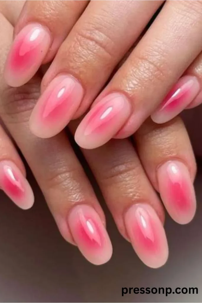 Close-up of medium-length oval nails featuring a high-gloss aura manicure with a bright pink gradient center bleeding into a milky nude base.