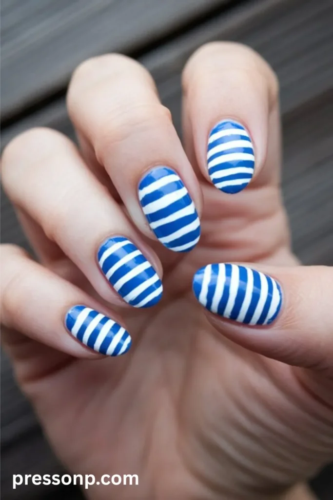 Close-up of medium-length oval nails painted with a glossy, alternating pattern of horizontal blue and white nautical stripes.