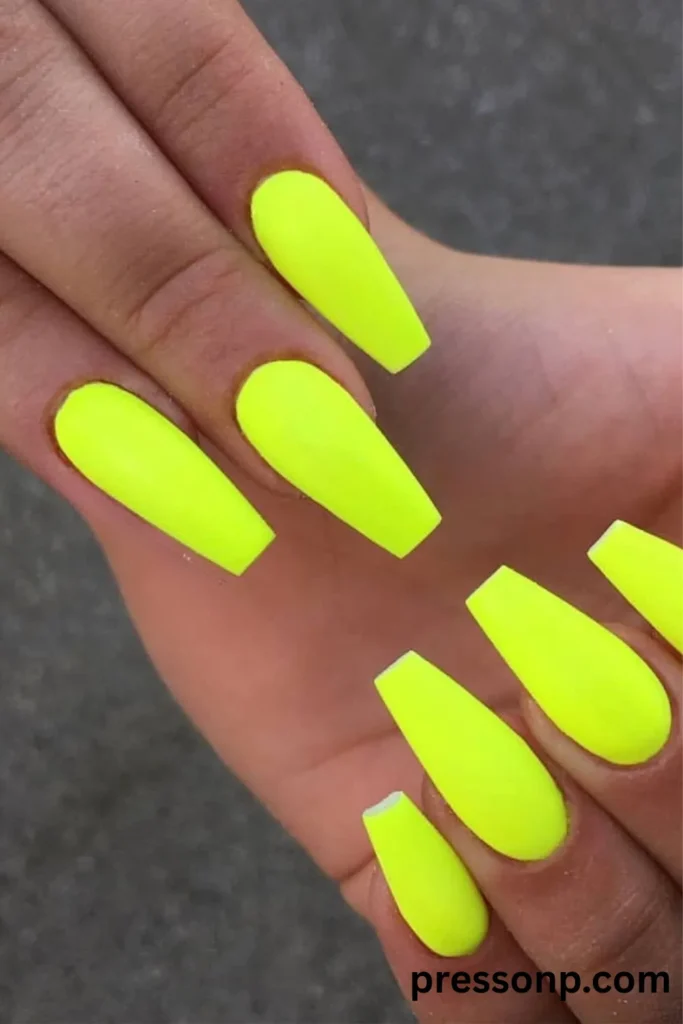 Close-up of long, sleek coffin-shaped nails painted in a solid, high-impact matte bright neon yellow polish.