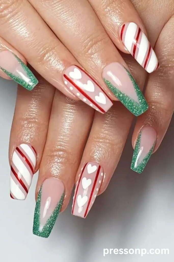 Close-up of long coffin-shaped nails with a glossy top coat, featuring a candy-themed manicure with red and white candy cane stripes, green glitter French tips, and white heart accents.